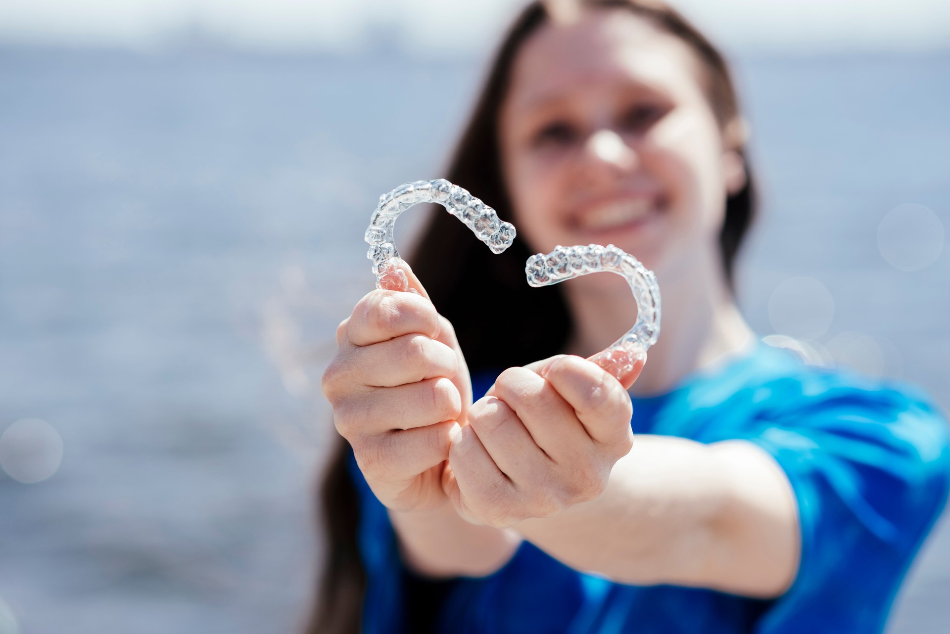 Dental care. Smiling beautiful woman holding heart-shaped aligners. Plastic retainers for teeth alignment.
